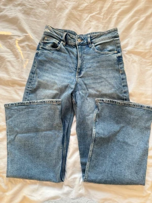 Ljusblå raka jeans med hög midja - Säljer ett par ljusblå jeans med rak passform och hög midja. Klassisk femficksmodell med dragkedja och knapp framtill. Jeansen har en avslappnad vibe och är tillverkade i denim. Perfekta till sneakers eller boots.