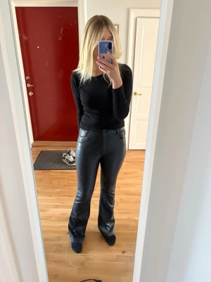Svarta utsvängda byxor i skinnimitation - Säljer ett par svarta byxor i skinnimitation med utsvängda ben och hög midja. Snygg passform som sitter tight upptill och släpper nedtill.