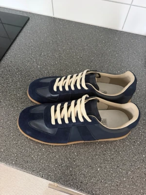 Gats (MVT) - Stilrena marinblå sneakers med beige gummisula och vita snören. Ovandelen är i en mix av mocka och slätt läder för en schysst kontrast. Insidan är ljus och skön, perfekt för dig som gillar klassisk men modern stil. Köpt från Oopbuy 