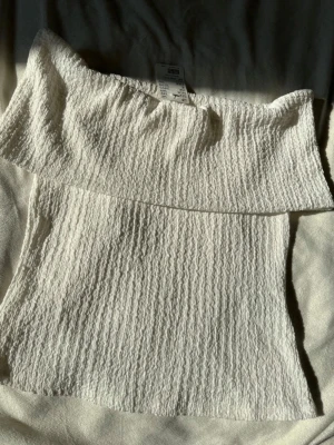 Vit offshoulder tubtopp - Säljer en snygg vit offshoulder tubtopp med struktur i tyget. Toppen är ärmlös och har en croppad passform som passar perfekt till höga jeans eller kjol. Superenkel att styla och ett måste i garderoben!