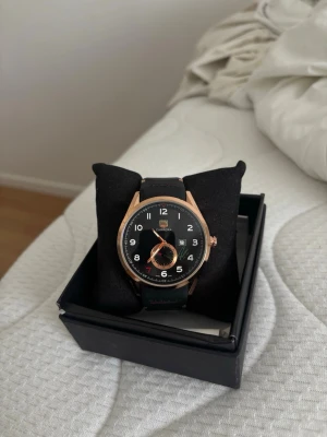 TAGHeur klocka  - Stilren klocka med svart urtavla och armband samt detaljer i roséguld. Urtavlan har tydliga vita siffror och en mindre sekundvisare. Klockan har ett klassiskt runt format och armbandet är i syntetmaterial. Perfekt accessoar för dig som vill ha en modern look.