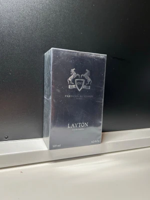Parfums de Marly Layton 125 ml - Exklusiv parfym från Parfums de Marly, modellen Layton. Flaskan rymmer 125 ml och kommer i en elegant, mörkblå förpackning med silverdetaljer och två hästar på logotypen. En lyxig doft som utstrålar klass och modernitet.