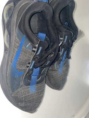 Nike Air Max 2021  - Säljer ett par svarta Nike sneakers som går för 1200 Nypris. Ovandelen är i mesh och textil med svarta och blå snören. Sulan är tjock och har synliga luftkuddar på sidan. Perfekta för dig som gillar sportig och modern stil.
