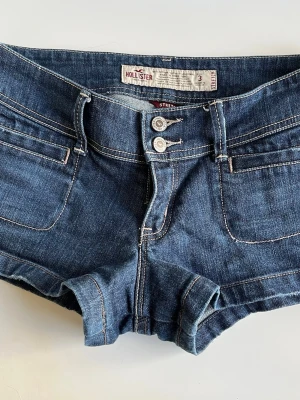 Mörkblå low waisted shorts från Hollister - Snygga mörkblå low waisted shorts från Hollister med dubbla knappar och klassiska fickor både fram och bak. Shortsen har kontrastsömmar och en lågmidjad passform som ger en avslappnad vibe. Perfekta för varma dagar och enkel att matcha med allt. Kan skicka fler bilder om det önskas! Storlek 3 men passar mig som ungefär är 34/36.