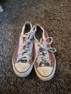 Rödvita Converse All Star låga sneakers - Klassiska Converse All Star sneakers i lågt snitt med röd och vit canvas, vita gummisulor och vita skosnören. Ikonisk stjärndetalj på tån och All Star-logga på plösen. Perfekta för en avslappnad och cool stil.