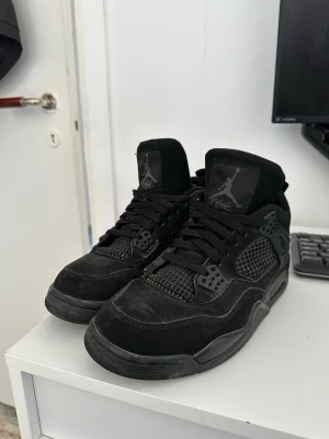 Jordan 4 black cats - Säljer ett par helsvarta Air Jordan 4 Retro sneakers med klassisk mesh och läderdetaljer. Skorna har högt skaft, ikonisk Jumpman-logga på plösen och hälen samt robust sula. Perfekta för dig som gillar streetwear och vill ha en tidlös look.