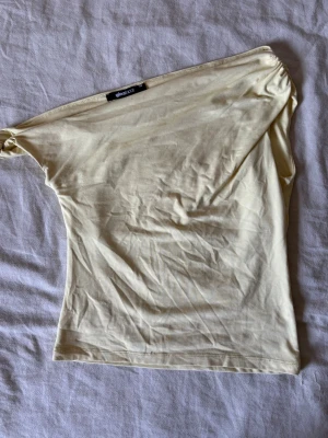 Ljusgul oneshoulder topp - Trendig ljusgul topp i oneshoulder-modell med enkel, slät design. Tillverkad i mjukt material som känns skönt mot huden. Perfekt för dig som vill ha en stilren och modern look.