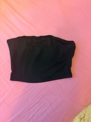 Svart bandeau tubtopp - Enkel och stilren svart bandeau tubtopp i mjukt material. Perfekt att matcha med höga jeans eller kjol för en clean look. Ärmlös och axelbandslös design som sitter bekvämt på plats.