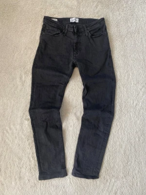 Svarta slim fit jeans - Säljer ett par svarta slim fit jeans med klassisk femficksdesign och normal midja. Jeansen har smal passform hela vägen ner och är tillverkade i stretchigt denimtyg för extra komfort. Perfekta till en avslappnad streetstyle-look.