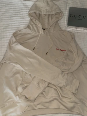 Beige hoodie med röd text - Säljer en beige hoodie med huva och dragsnören. På bröstet finns broderad röd text som säger 'It's Famous'. Hoodien har en klassisk känguruficka och ribbade muddar vid ärmslut och nederkant. Perfekt för en chill och avslappnad stil. Strl S men lite oversize 🔥