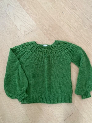 Grön stickad tröja från Carin Wester - Säljer en grön stickad tröja med rund hals och snyggt strukturmönster upptill. Tröjan har långa ballongärmar och ribbade muddar vid ärmslut och nederkant. 