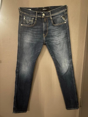Replay Jeans - Tja! Jag säljer ett par snygga mörkblå slim fit jeans från Replay med klassisk femficksdesign och kontrastsömmar. Jeansen har en lätt tvättad look med slitningar på låren och smal passform. Perfekta för en trendig och avslappnad stil. Det är bara och skicka vid funderingar:)