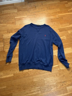 Blå långärmad tröja från Polo Ralph Lauren - Mörkblå långärmad tröja från Polo Ralph Lauren med rund halsringning och den klassiska röda loggan broderad på bröstet. Tröjan är i mjuk bomull och har ribbade muddar vid ärmslut och nederkant. Storlek L 