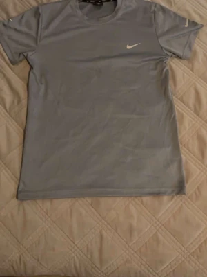 Ljusblå Nike t-shirt i bomull - Snygg ljusblå t-shirt från Nike med klassisk logga på bröstet. T-shirten har rund halsringning och korta ärmar. Tillverkad i mjuk bomull som känns skön mot huden. Perfekt för en sportig och avslappnad stil.