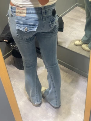 Ljusblå bootcut jeans true religion med fickdetaljer - Säljer ett par ljusblå bootcut jeans med fickdetaljwr. Från true religion! Köpta för 1299kr. !!kolla sista bild för se defekt!! Dem är alltså nersydda men går lätt att sy upp!💕 w27