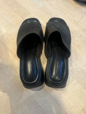 Svarta platåsandaler från Vagabond - Säljer ett par svarta platåsandaler från Vagabond med bred rem i skinn och öppen tå. Sandalerna har chunky sula och slip-in modell som ger en cool och trendig look. Perfekta för dig som gillar minimalistisk stil och vill ha lite extra höjd.