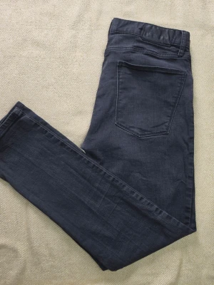 J.Lindeberg Damien Edge jeans svart storlek W36 L32 - Svarta jeans från J.Lindeberg i modellen Damien Edge. Mid-rise med Skinny Fit och stretchmaterial. Klassisk femficksmodell med diskret J.Lindeberg-logotyp på myntfickan.  Storlek W36 L32 Damien Edge Mid-Rise / Skinny Fit  Bra begagnat skick med normalt bruksslitage och viss blekning. Mindre ljust märke framtill, se bilder för detaljer.  Mått Midja: ca 42 cm Grenhöjd: ca 24 cm Ytterbenslängd: ca 100 cm Innerbenslängd: ca 76 cm Benvidd nedtill: ca 15cm  Material 98% bomull 2% elastan