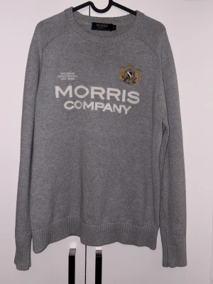 Grå tröja från Morris Company - Snygg grå tröja från Morris Company med broderad logga och text framtill. Tröjan har rund halsringning, långa ärmar och ribbade muddar. Perfekt för en stilren och avslappnad look.
