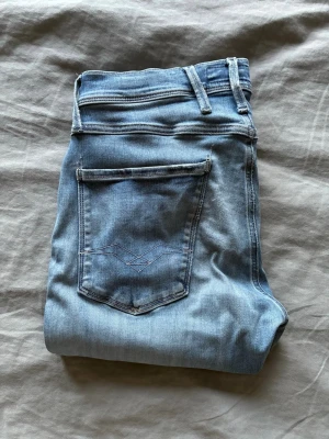 Ljusblå slim fit jeans Anbass 32 - Säljer ett par ljusblå slim fit jeans i modellen Anbass. Jeansen har klassisk femficksdesign, snygga slitningar och kontrastsömmar. Perfekta för dig som gillar en smalare passform och vill ha en fräsch, modern look. Hm: liten deffekt vid skrevet men kanske 1cm.