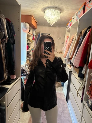 Svart långärmad skjorta i fake läder - Snygg svart skjorta i fake skinn med lång ärm och klassisk krage. Skjortan har knappar framtill och en figurnära passform. Perfekt att styla med jeans och är även snygg att ha som en lätt jacka nu till hösten ☺️