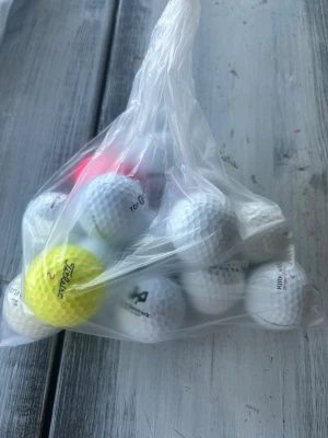 Påse med blandade golfbollar - En plastpåse fylld med flera golfbollar i olika färger, bland annat vita, en gul och en rosa. Bollarna har olika märken och tryck, och är tillverkade i klassiskt hårt material. Perfekt för dig som vill fylla på golfbolls-förrådet.