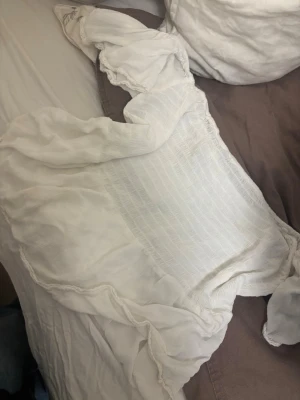 Vit offshoulder blus - Säljer en vit offshoulder blus  i storlek 34. Blusen har en smockad överdel och volangiga kanter, vilket ger en romantisk vibe. Tillverkad i ett tunt, luftigt tyg som känns perfekt för sommaren.