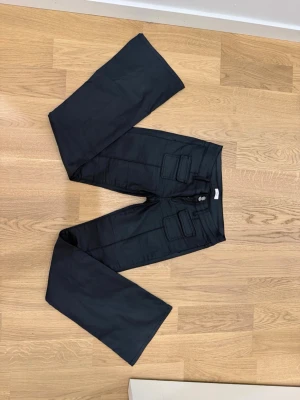 Svarta skinn imitations byxor  - Säljer ett par svarta skinn imitations byxor med bootcut ben två stora fickor framtill med lock. Byxorna har dubbla knappar i midjan och är tillverkade i ett slitstarkt tyg som ger en cool och avslappnad look. Finns lite slitningar där bak men inget som syns. Pris kan diskuteras 