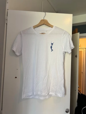 Vit ifk Göteborg T-shirt med blått tryck  - Säljer en vit t-shirt i bomull med en liten blå broderad figur på bröstet. T-shirten har rund halsringning och korta ärmar. Enkel och clean design som passar till det mesta. Nästan aldrig använd