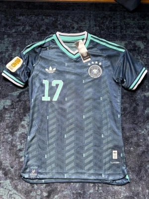 Germany Away kit WC 2026 - Snygg bortatröja från det tyska landslaget med spelare #17 florian wirtz. Helt ny med tags. Vm badge i guld och vit är tryckt på tröjan samt nummer och namn. Endast provad en gång. Slim fit storlek M (passar S och liten M) spelarversion som är slutsåld överallt.