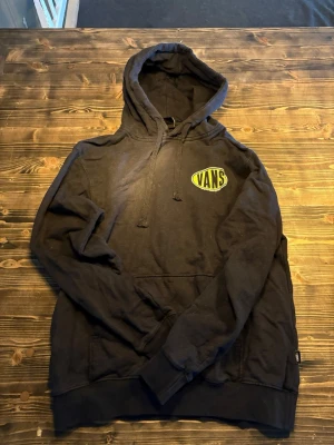 Svart Vans hoodie med gul logga - Säljer en svart hoodie från Vans med stor gul logga på ryggen och mindre logga på bröstet. Klassisk huva med dragsko och magficka framtill. Perfekt för dig som gillar streetwear och vill ha en skön och stilren hoodie.