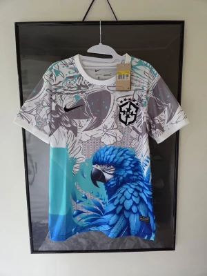 Fotbollströja Brasilien SPECIAL EDITION  - Unik och riktigt snygg Brasilien-inspirerad fotbollströja (Fantasy Kit / Special Edition) med mönster av en blå hyacintpapegoja och tropiska detaljer.  ​Storlek: Small (S) ​Skick: Helt ny och oanvänd med alla lappar kvar.
