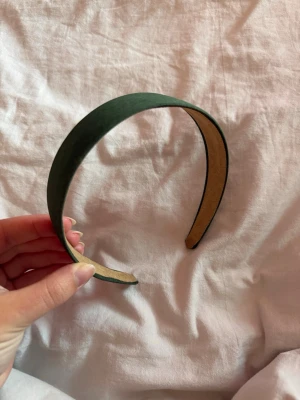 Mörkgrönt brett diadem i mockaimitation - Stilrent mörkgrönt diadem med bred form och mjuk mockaimitation på utsidan. Insidan är beige och har en slät yta som sitter bekvämt mot håret. Perfekt accessoar för att lyfta din look med en enkel touch av färg.