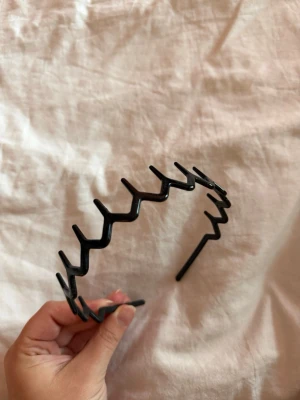 Svart hårband - Säljer ett svart hårband i plast med taggig, vågig design som håller håret på plats. Perfekt för dig som vill ha en enkel look. Lätt och bekvämt att bära hela dagen.