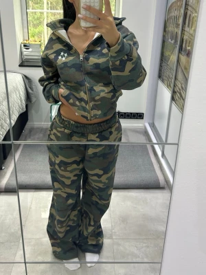 Camouflage hoodie med dragkedja - Säljer en camouflagemönstrad hoodie med dragkedja och huva. Hoodien har en vit stjärnlogga på bröstet och är i mjukt material. Perfekt för en chill och avslappnad stil. 
