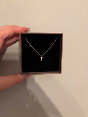 Guldhalsband med T-bokstav från Edblad - Snyggt och stilrent halsband i guld från Edblad med ett litet T som hänge. Kedjan är tunn och elegant, perfekt för dig som gillar minimalistiska smycken. Kommer i original ask. Färg: Guld💗
