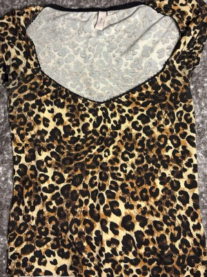 Leopardmönstrad topp med v-ringning - Snygg topp med leopardmönster i bruna, svarta och beige toner. Modellen har korta ärmar och en djup v-ringning framtill. Materialet känns stretchigt och lätt, perfekt för att sticka ut lite extra.