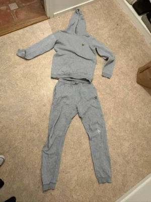 Grå mjukisbyxor med logga - Snygga grå mjukisbyxor med resår i midjan och muddar vid bensluten. Byxorna har en liten gul logga på vänster sida och är gjorda i mjukt bomullsmaterial. Perfekta för chill dagar eller när du vill vara extra bekväm.