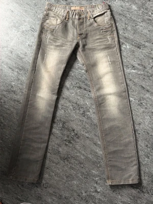 Gråa jeans från Fadnoble Jeans 2002 - Snygga gråa jeans med slitna detaljer och raka ben från Fadnoble Jeans 2002. Jeansen har klassisk femficksmodell och kontrastsömmar. Perfekta för en avslappnad och trendig look.