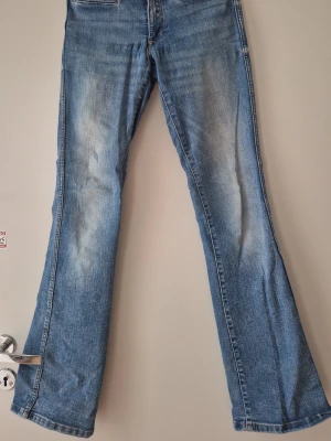 Blå bootcut jeans med slitningar - Ett par klassiska blå bootcut jeans med lätt slitna detaljer framtill. Jeansen har normalhög midja, fem fickor och dragkedja med knapp. Materialet är denim i bomull med en skön känsla och snygg tvätt.