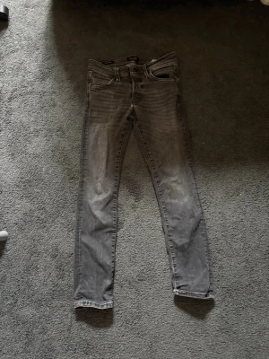 Grå slim fit jeans med slitningar - Snygga grå slim fit jeans med lätt slitna detaljer och klassisk femficksdesign. Jeansen har smal passform och normal midja, perfekta för en avslappnad och trendig look. Materialet ser ut att vara bomullsdenim med lite stretch.