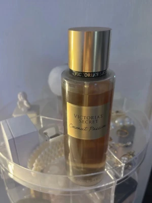 Victoria's Secret Coconut Passion parfym - En lyxig parfym från Victoria's Secret i doften Coconut Passion. Flaskan är cylindrisk med guldfärgat lock och etikett. Innehållet har en varm, gyllene ton och flaskan är tillverkad i genomskinlig plast. Perfekt för dig som älskar tropiska och söta dofter.