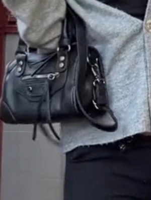 Svart handväska med nitar och dragkedja - Snygg svart handväska i skinnimitation med silverfärgade nitar och detaljer. Väskan har dubbla handtag, dekorativ dragkedja framtill och en cool, lite rockig look. Perfekt storlek för det viktigaste och passar till många olika outfits.