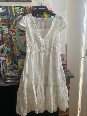 Vit prickig klänning med spetsdetaljer - Söt vit kortklänning från Vintage stories med små diskreta prickar. Klänningen har v-ringning, korta ärmar och volang nedtill. Tillverkad i ett lätt och luftigt material, perfekt för varma dagar. Passar dig som gillar en romantisk och avslappnad stil. Bomulls material och med vit underklänning som följer med till.