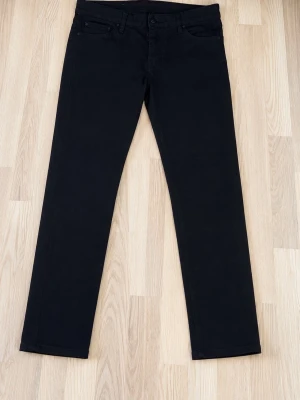 Svarta raka jeans herr Desquared  - Snygga svarta jeans med rak passform och klassisk femficksdesign. Jeansen har normal midja och stängs med dragkedja och knapp. Perfekta till en avslappnad stil och funkar året runt. Materialet är troligtvis bomull med lite stretch för extra komfort.
