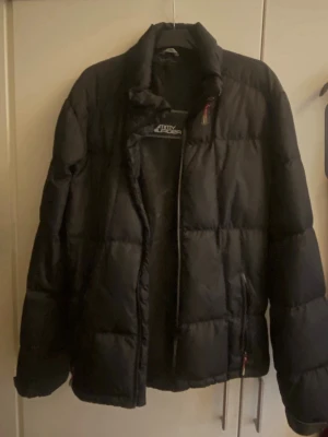Svart dunjacka från Tommy Hilfiger  - Säljer en svart dunjacka från Tommy Hilfiger med hög krage och dragkedja framtill. Jackan har en klassisk quiltad design och två sidofickor med dragkedja. Perfekt för kalla vinterdagar och riktigt skön att bära. Kan behövas puffas till annars i bra skick samt namnet har börjat blekna lite annars perfekt.
