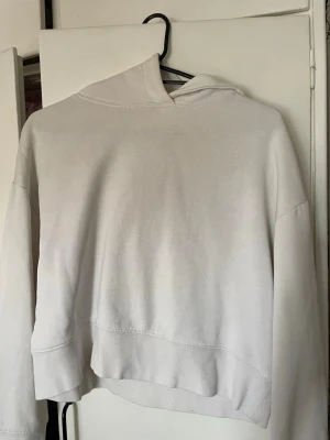Vit hoodie med huva - En enkel och stilren vit hoodie med huva. Hoodien har en avslappnad passform och är tillverkad i mjukt material, perfekt för chill dagar. Inga synliga tryck eller loggor, bara clean och basic design. Har lite missfärgningar men går bort i tvätt