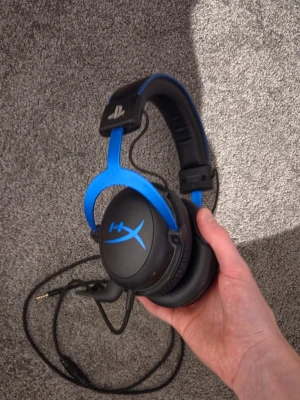 HyperX gaming headset blå/svart - Säljer ett HyperX gaming headset med blå detaljer och svart vadderad bygel. Over-ear design med mjuka öronkuddar och PlayStation-logga på bygeln. Kabelanslutning med 3,5mm kontakt, perfekt för gaming och långa sessions. Dom funkar som dom ska har ett par nya därför jag säljer dom kan dubbel kolla så dom funkar innan jag skickar