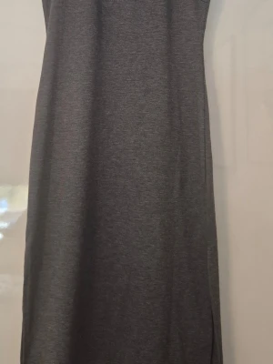Grå långklänning i bomull - En enkel och stilren grå långklänning i mjukt bomullsmaterial. Klänningen har en rak passform och är ärmlös, perfekt för en avslappnad och bekväm look. Passar till många olika tillfällen och är lätt att matcha med accessoarer.