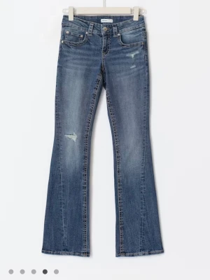 Gina blå bootcut jeans med slitningar - Snygga blå bootcut jeans med lätt slitna detaljer på låret och knät. Jeansen har klassisk femficksmodell och knappgylf. Tillverkade i denim med en tvättad look som ger en avslappnad känsla.