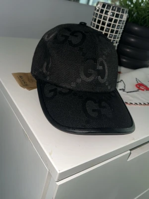 Svart keps med GG-mönster - Snygg svart keps med tydligt GG-mönster över hela kepsen. Kepsen har böjd skärm och är tillverkad i ett slitstarkt tygmaterial. Perfekt för dig som vill ha en stilren accessoar med exklusiv känsla.